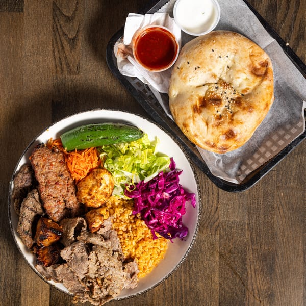 Turkish mixed grill platter with gyro, kebab, rice, salad, and flatbread on a wooden table.