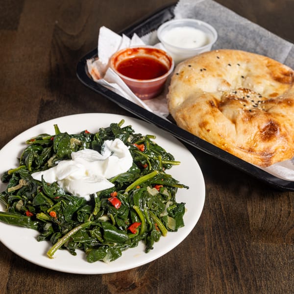 Turkish spinach with yogurt and red peppers, alongside flatbread, red sauce, and white sauce.