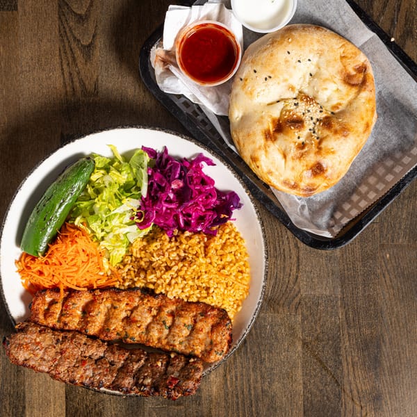 Turkish Adana kebab plate with bulgur, salad, grilled pepper, and flatbread with sauces.