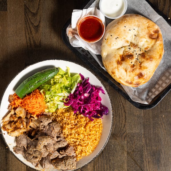 Turkish gyro and kebab plate with rice, meat, vegetables, and flatbread on a wooden table.