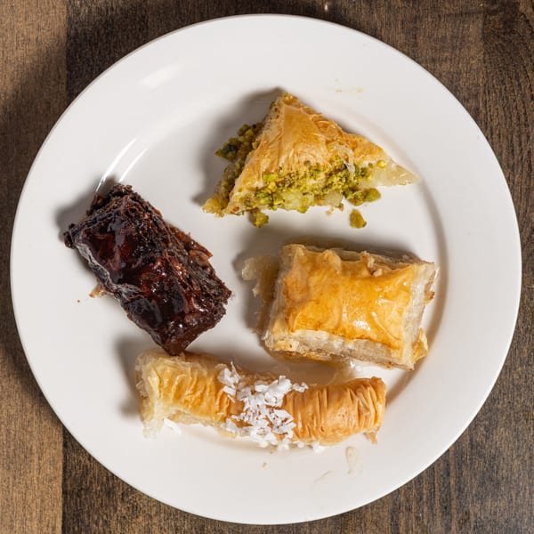A white plate holds four pieces of Turkish baklava, including pistachio, chocolate, and coconut varieties.