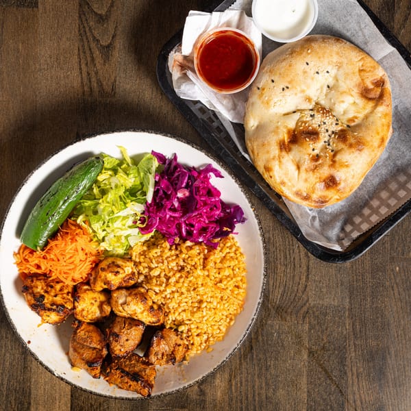 Turkish chicken kebab plate with rice, salad, grilled pepper, flatbread, and sauces on a wooden table.